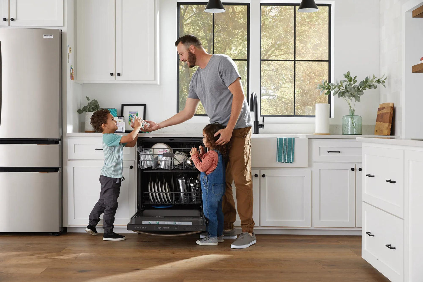 Man unloading open built-in dishwasher with two children in bright modern kitchen with stainless appliances