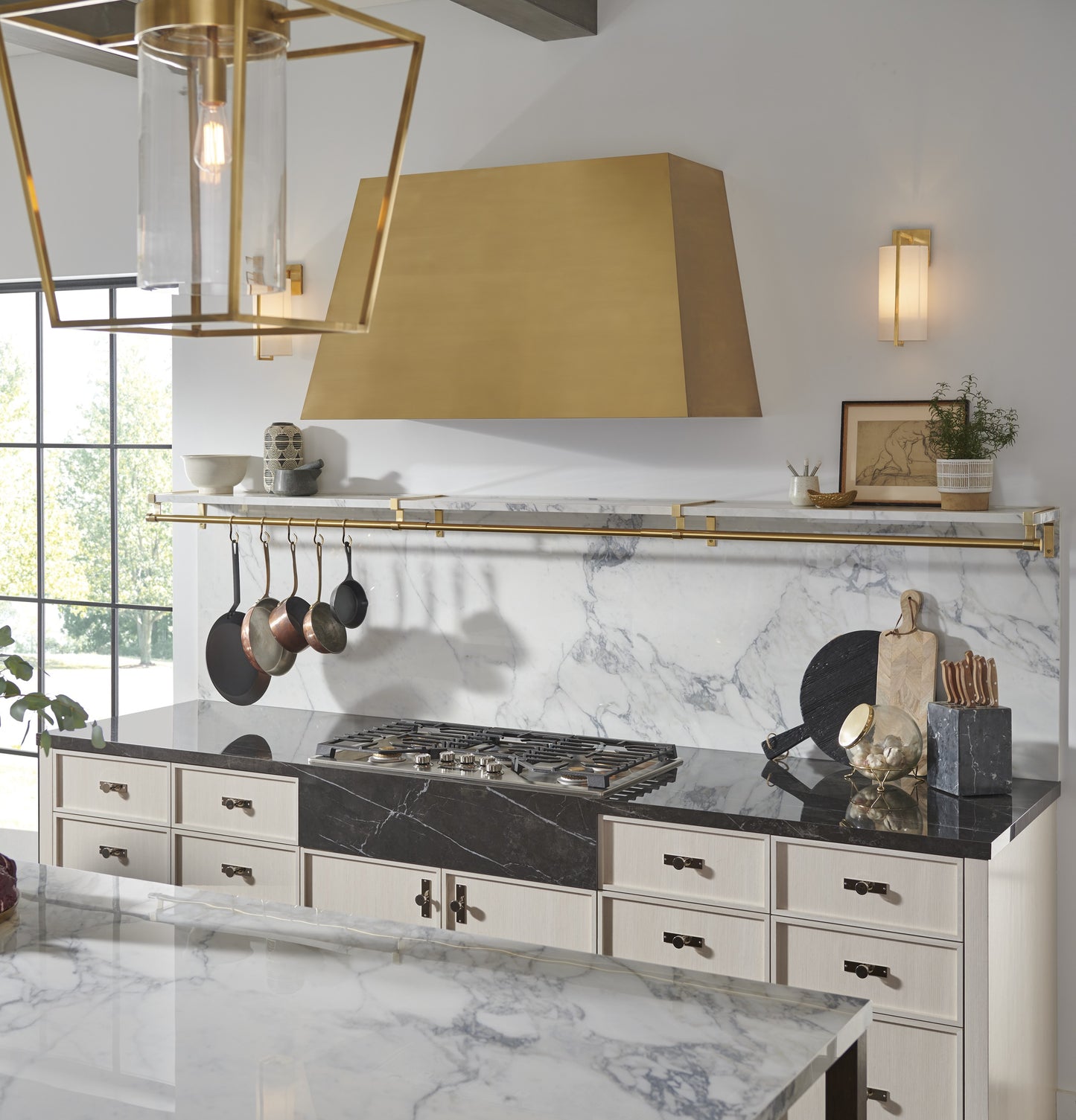 Modern brass kitchen hood above marble backsplash with hanging cookware in Over the Range Hoods and Kitchen & Kitchenware collections