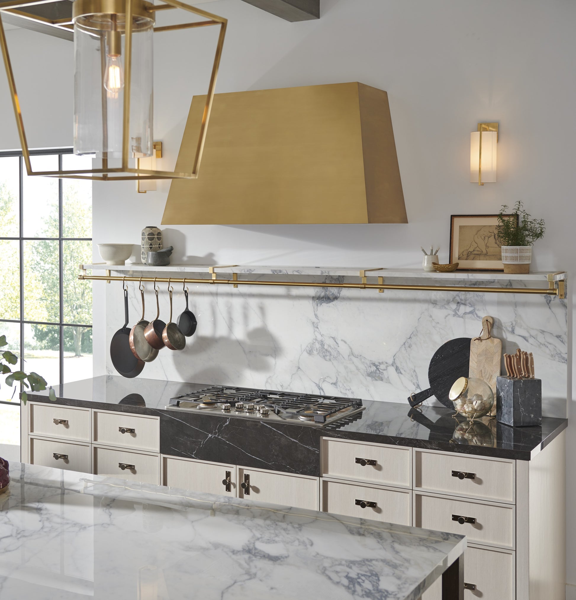 Modern brass kitchen hood above marble backsplash with hanging cookware in Over the Range Hoods and Kitchen & Kitchenware collections