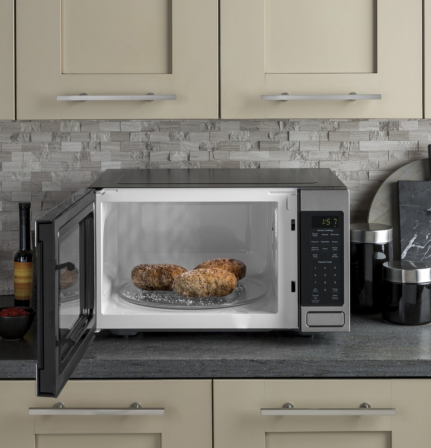 Countertop microwave with open door heating three baked potatoes on rotating glass tray in modern kitchen setting