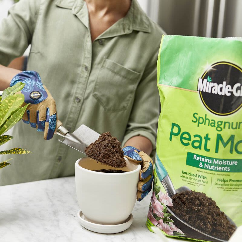 Gardener wearing gloves scooping peat moss into a white flowerpot for home improvement and gardening tasks