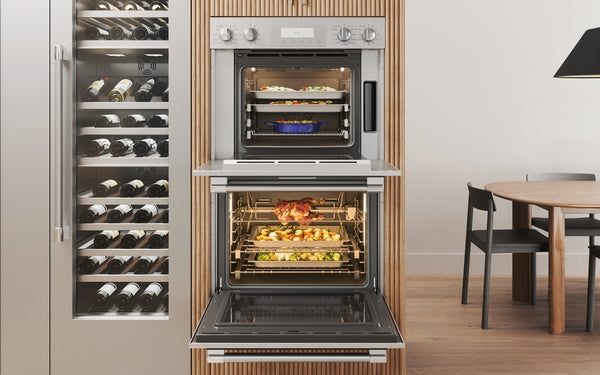 Stainless steel double steam wall oven with open doors showing roasting chicken and baked dishes in modern kitchen setting