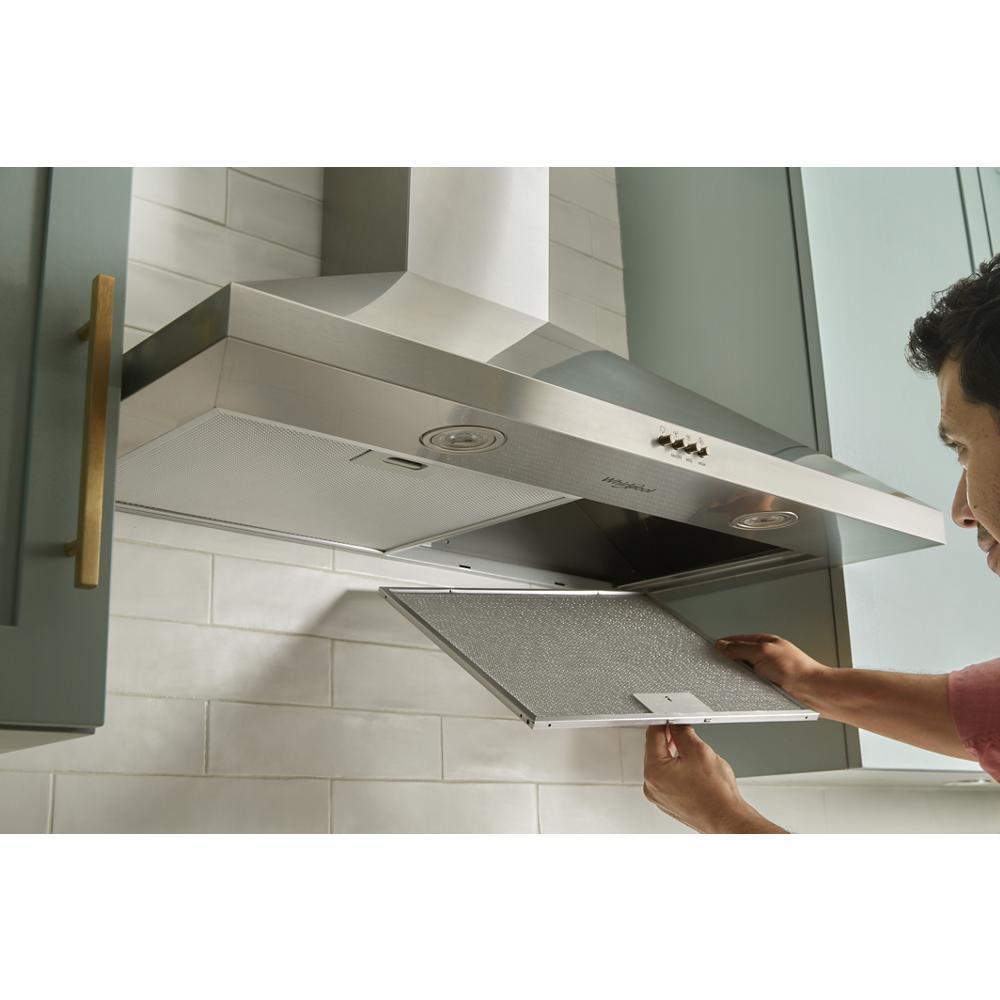 Person removing detachable grease filter from stainless steel chimney wall mount range hood in modern kitchen setting