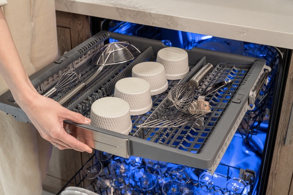 Pull-out utensil rack inside stainless steel dishwasher illuminated with blue light from Thermador appliances collection