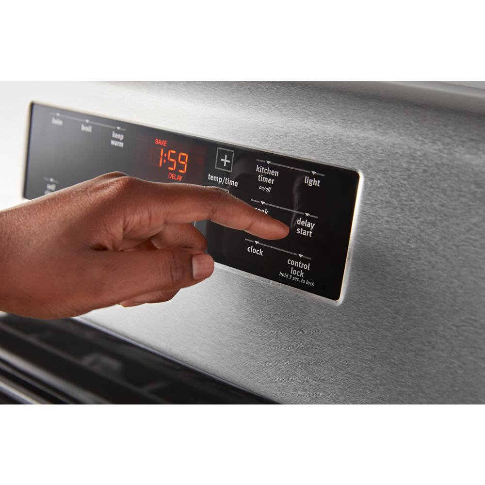 Person adjusting the digital control panel on a stainless steel electric range for kitchen appliance use