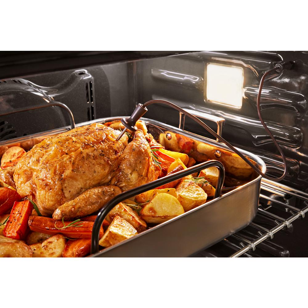 Roast chicken with carrots and potatoes inside stainless steel oven with interior light on