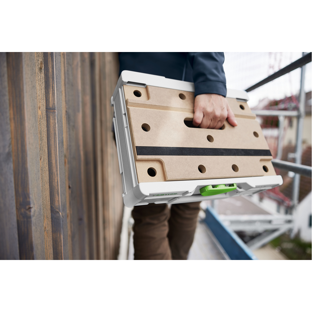 Person carrying a compact Festool modular storage box with a perforated wooden lid and white frame, ideal for workshop organization and tool storage.