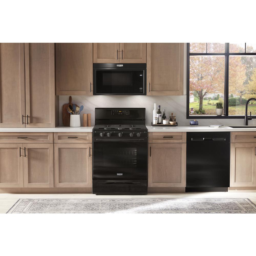 Black built-in over-the-range microwave above black gas stove in modern kitchen with wood cabinets and large window