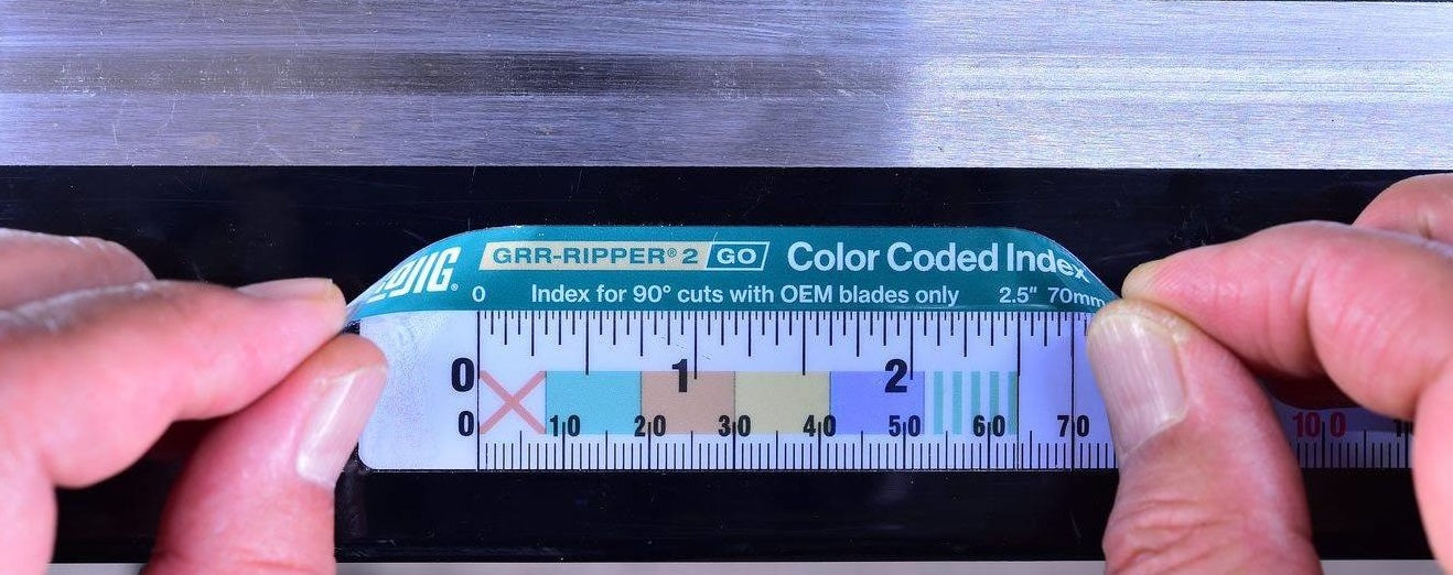 Hands holding a Microjig GRR-RIPPER2 Go Push Block safety tool with measurement markings on a table saw guide rail