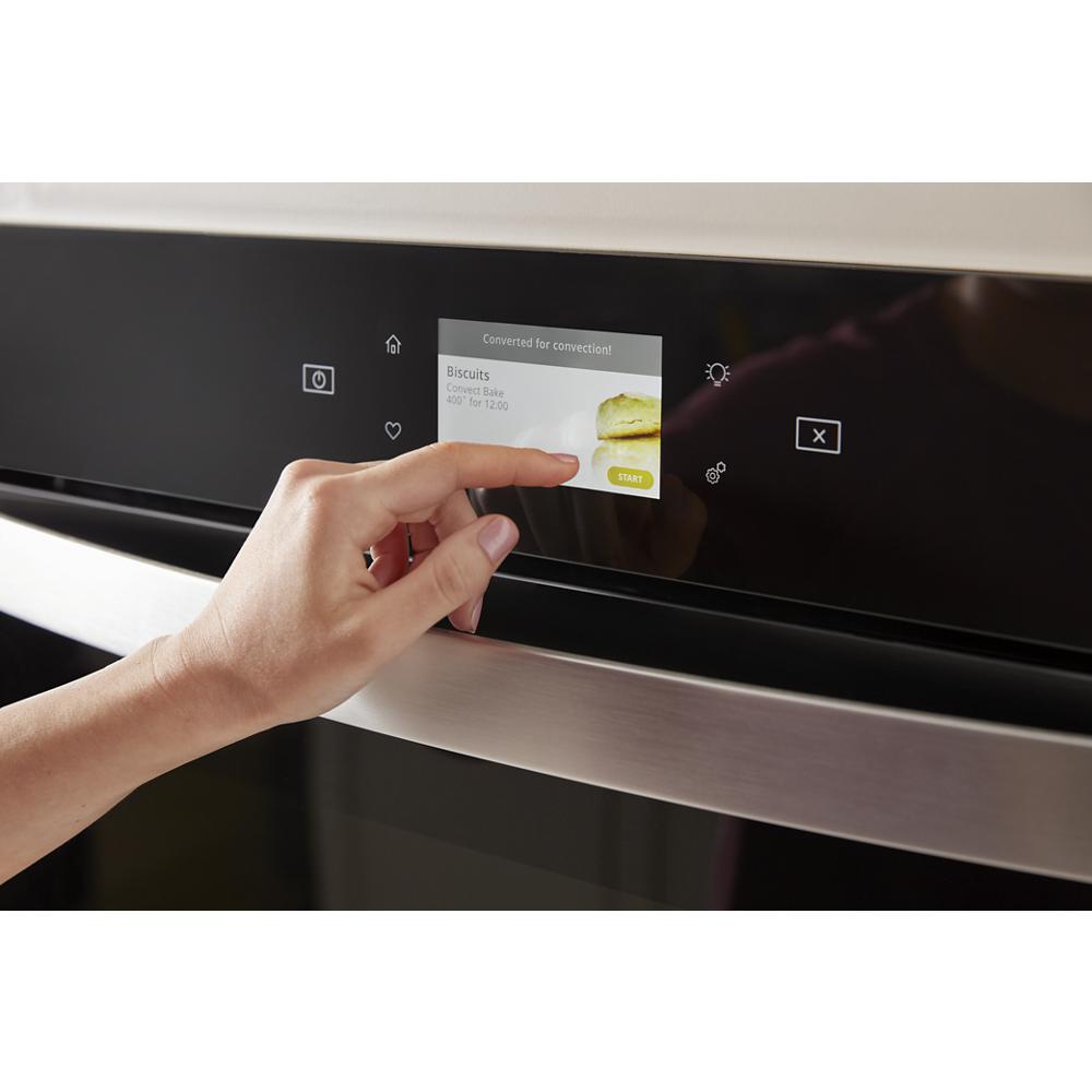 User interacting with the digital touchscreen control panel of a stainless steel wall oven microwave combo in modern kitchen appliances.