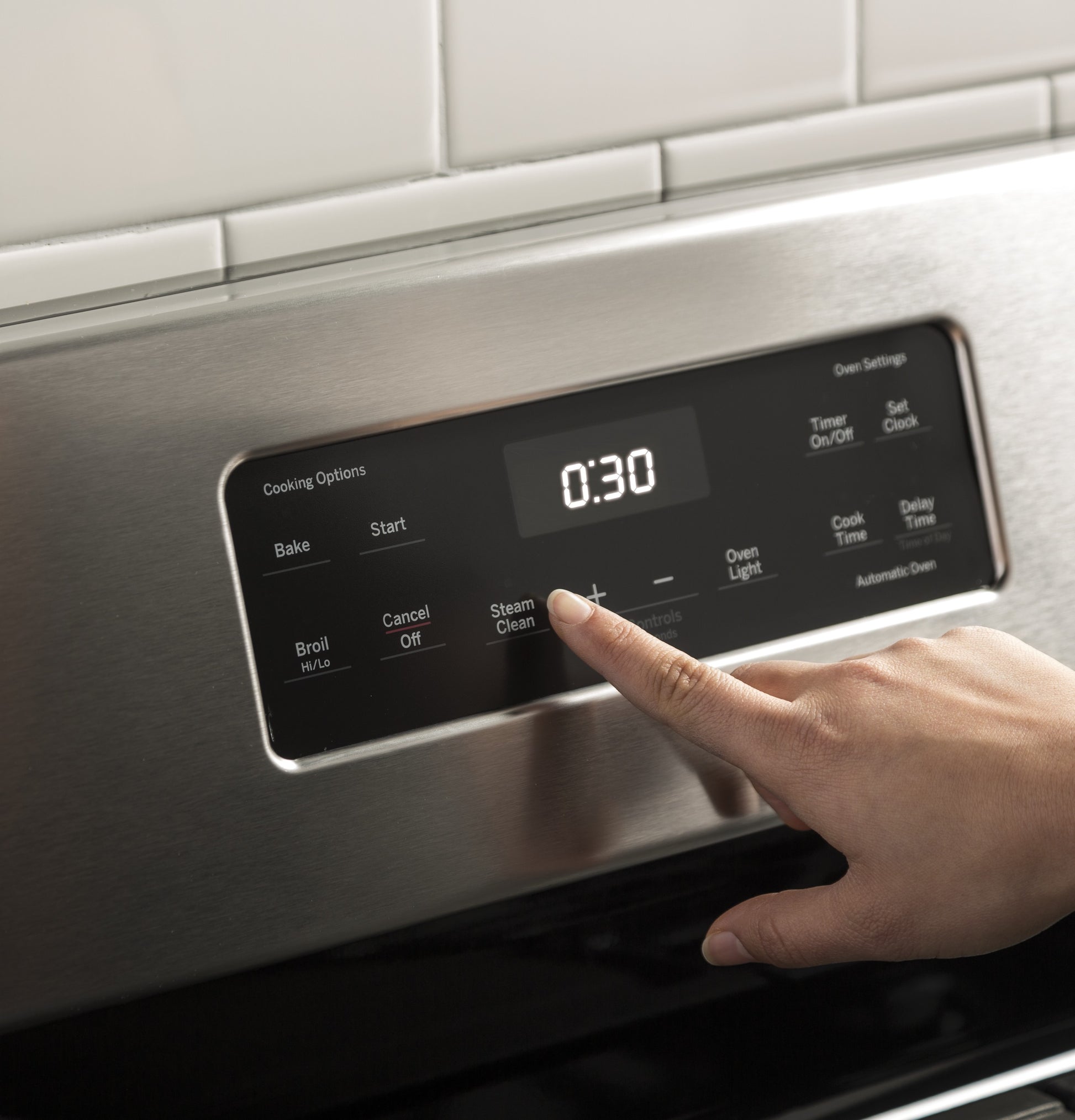 Finger pressing steam clean button on stainless steel control panel of freestanding gas range timer set to 30 minutes