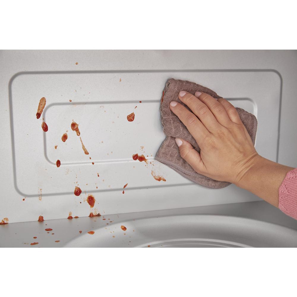 Hand wiping sauce splatters inside a microwave cavity with a brown cloth in kitchen appliances cleaning context