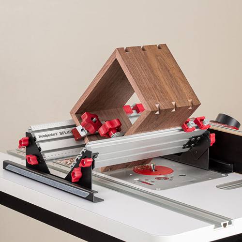 Aluminum spline jig with red knobs holding wooden box frame on router table for accurate woodworking joinery cuts