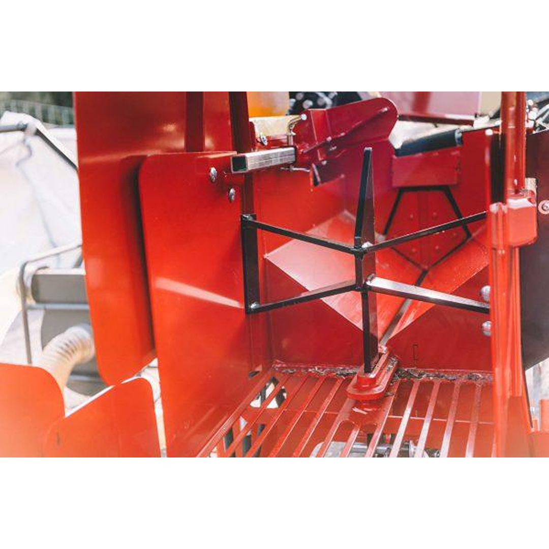 Close-up of red firewood processor’s mechanical splitting mechanism with black metal log holder in outdoor setting