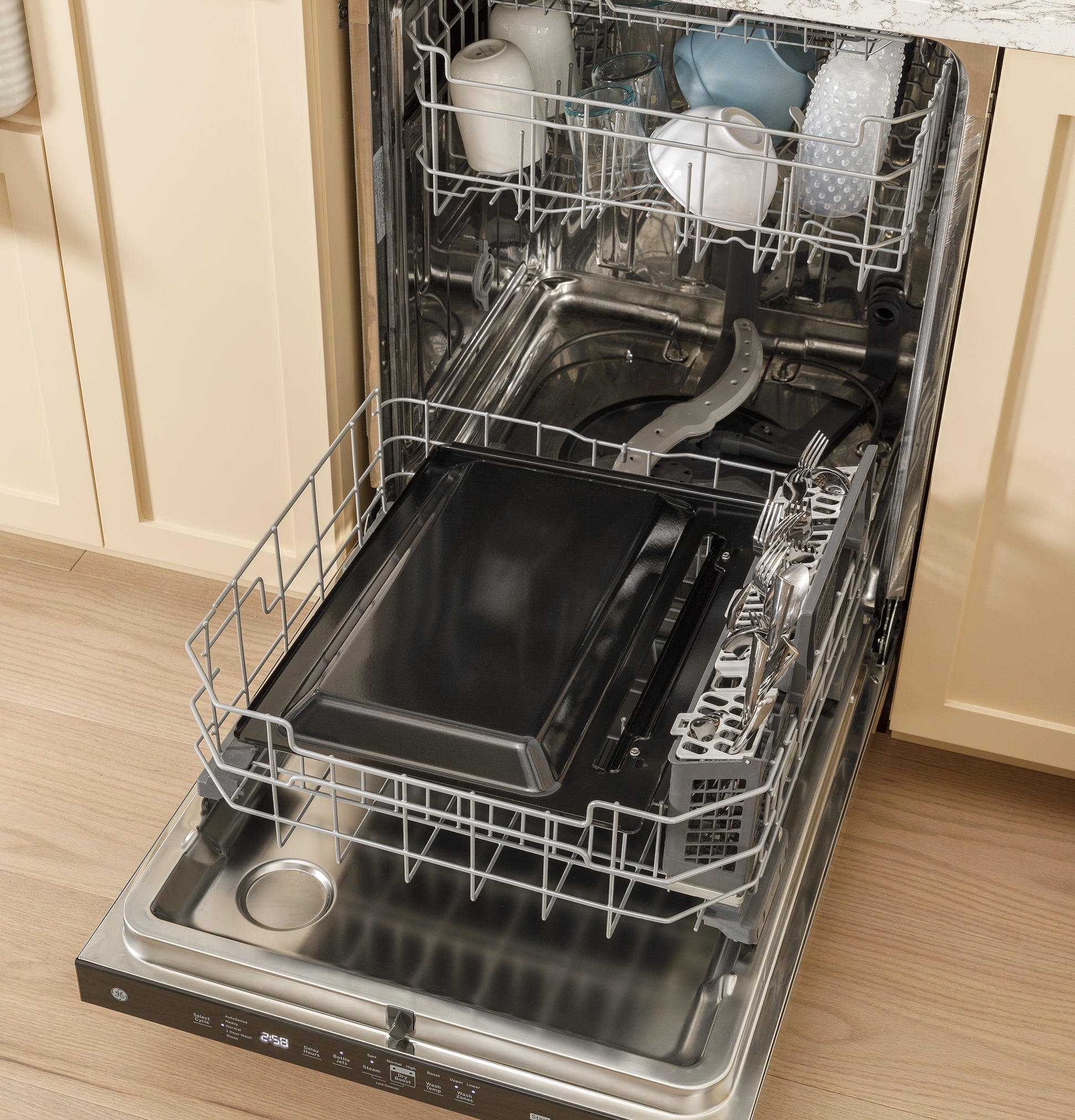 Black EasyWash™ oven tray placed on lower rack of stainless steel dishwasher open in kitchen setting