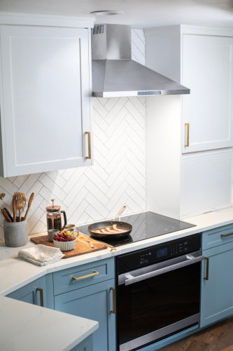 Modern kitchen with built-in electric wall oven, blue lower cabinets, white upper cabinets, and stainless steel vent hood.