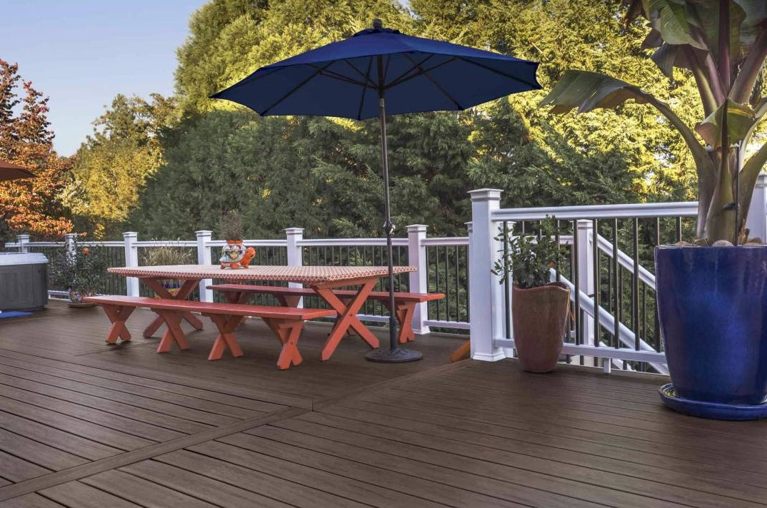 Outdoor deck with dark roast grooved composite boards, wooden picnic table, and blue patio umbrella for home improvement