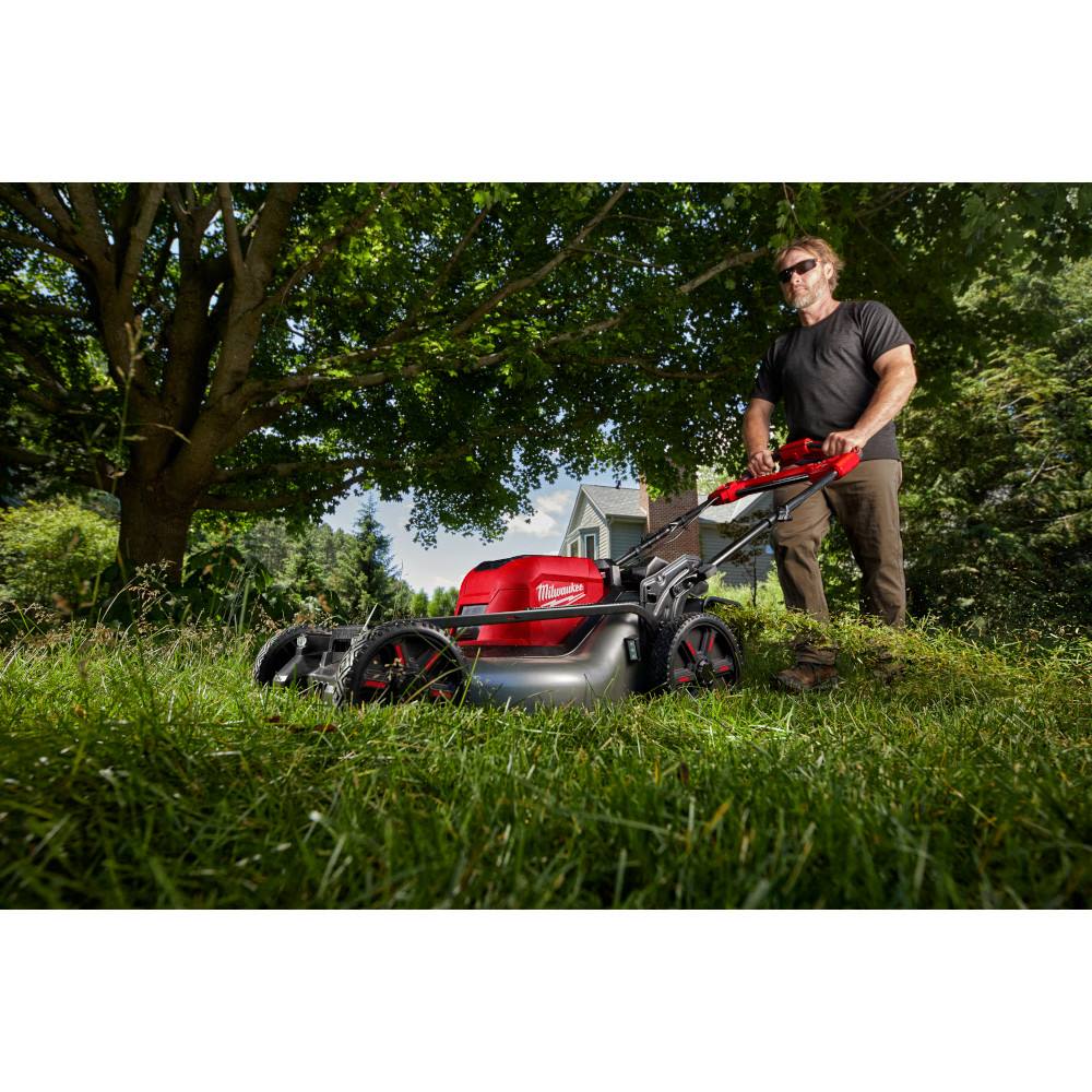 Man using red and black self-propelled mower with dual batteries for outdoor lawn maintenance tasks