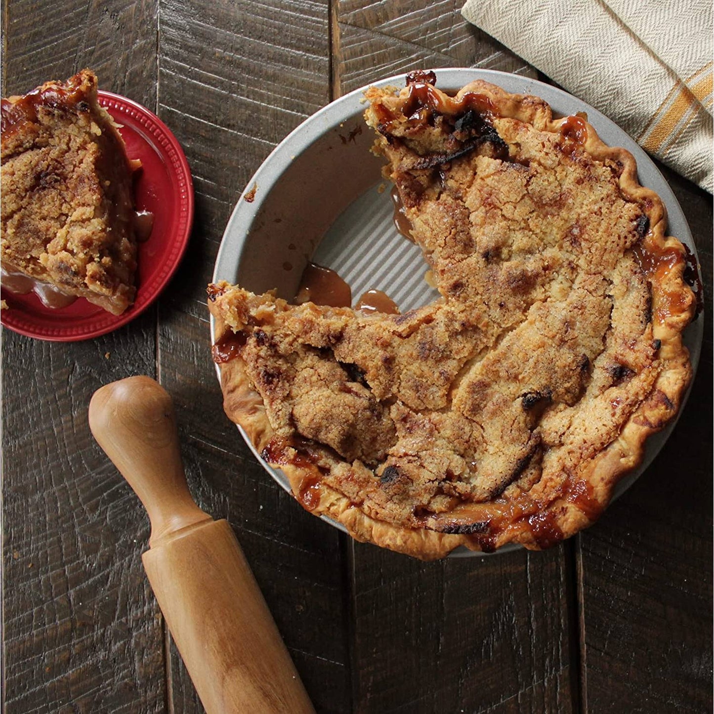 Partially eaten crumb-topped pie baked in a 9-inch metal pie pan on a rustic wood surface with rolling pin nearby