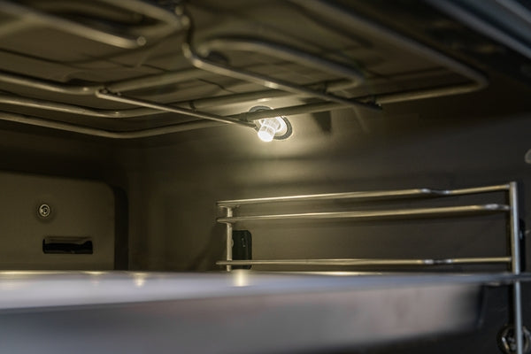 Interior view of stainless steel steam convection oven cavity with illuminated light and metal heating element rack