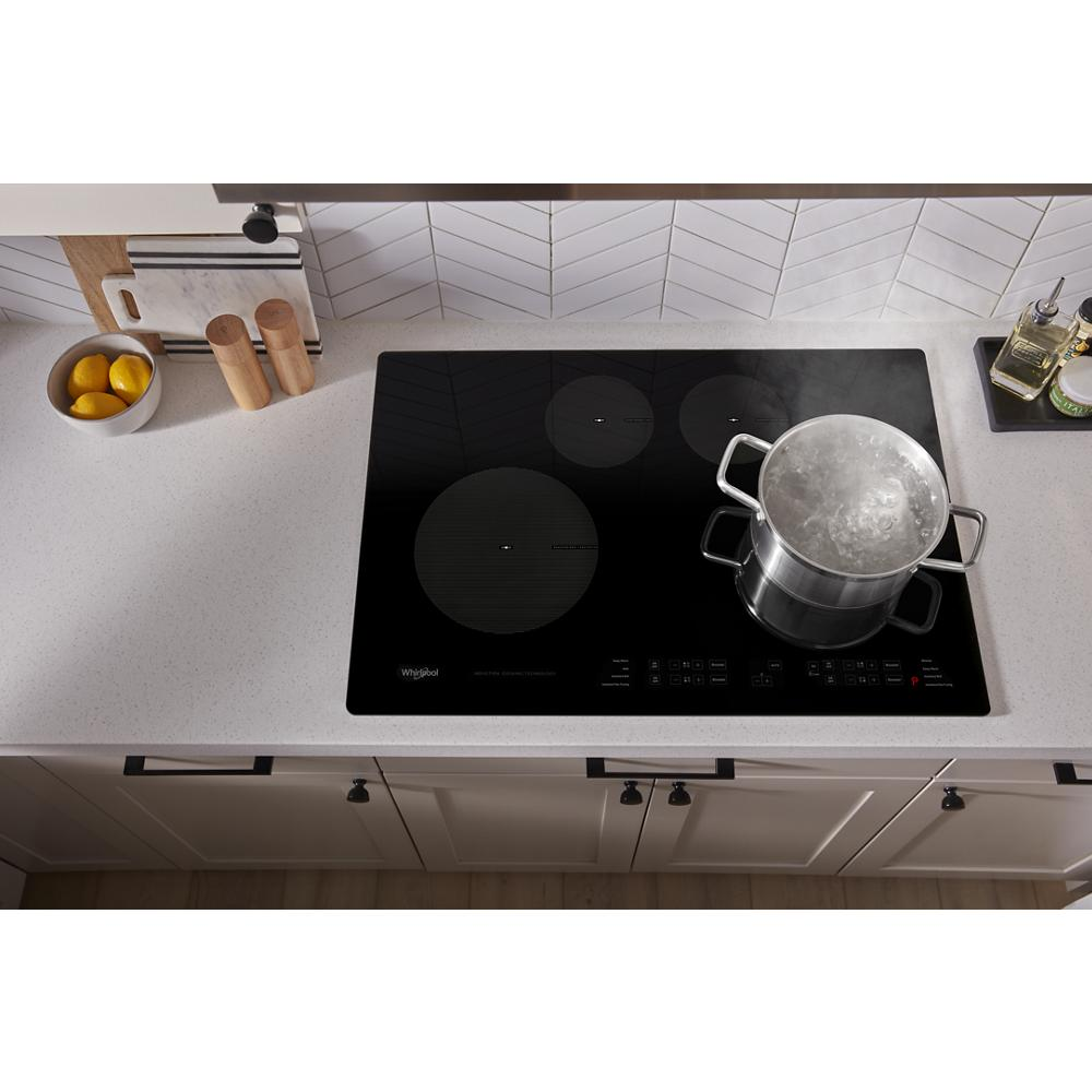 Black Whirlpool induction cooktop with three cooking zones boiling water in stainless steel pot on kitchen countertop