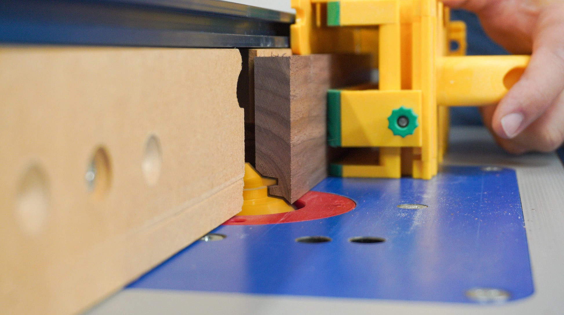 Close-up of yellow jig and router bit cutting precise lock miter joint on dark wood piece in woodworking setup