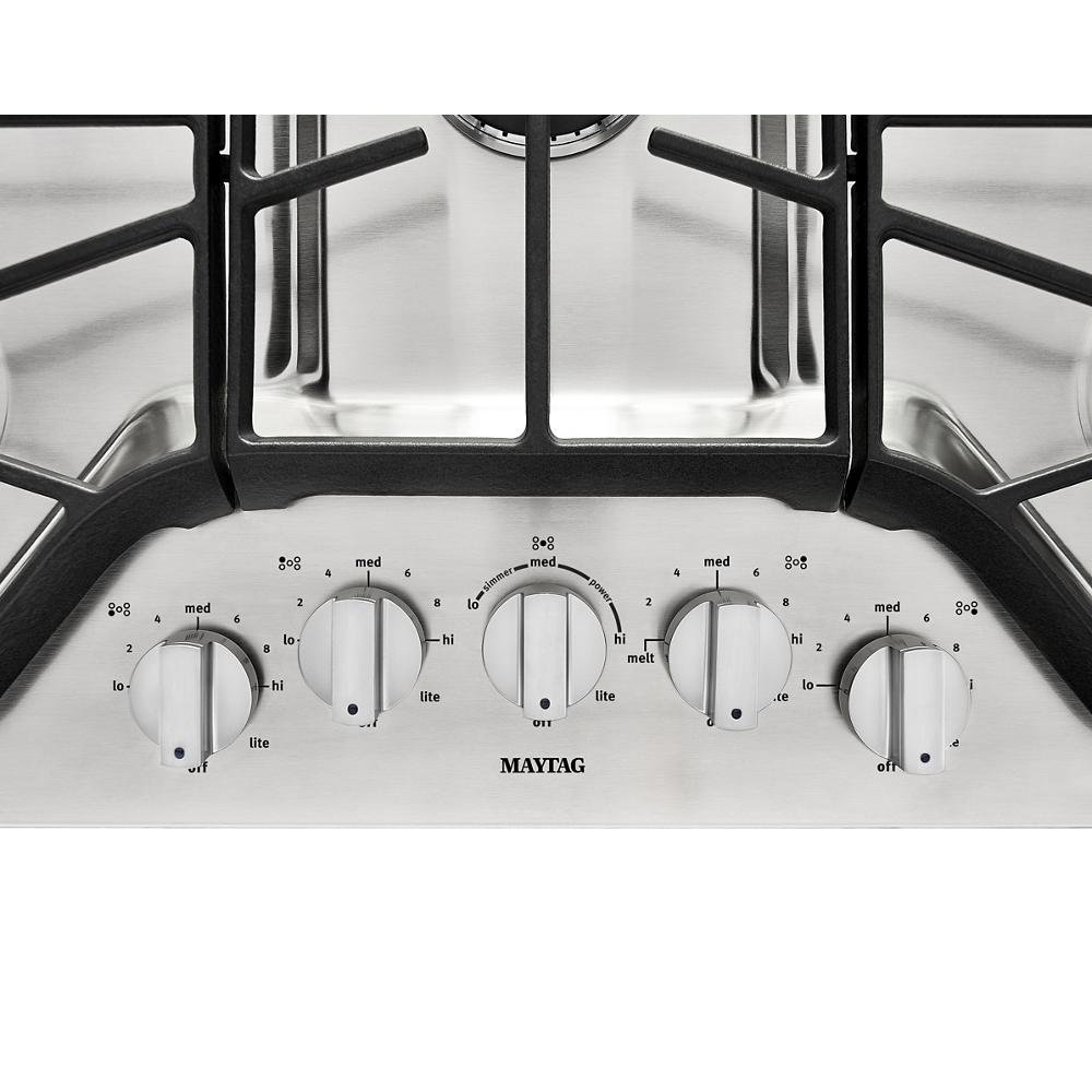 Control knobs panel on stainless steel cooktop with black cast iron grates, part of home improvement appliances collection