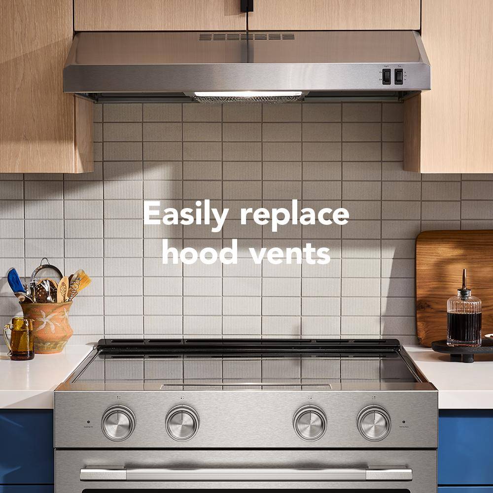 Stainless steel low profile microwave hood installed above modern stove in kitchen with wood cabinets and tiled backsplash