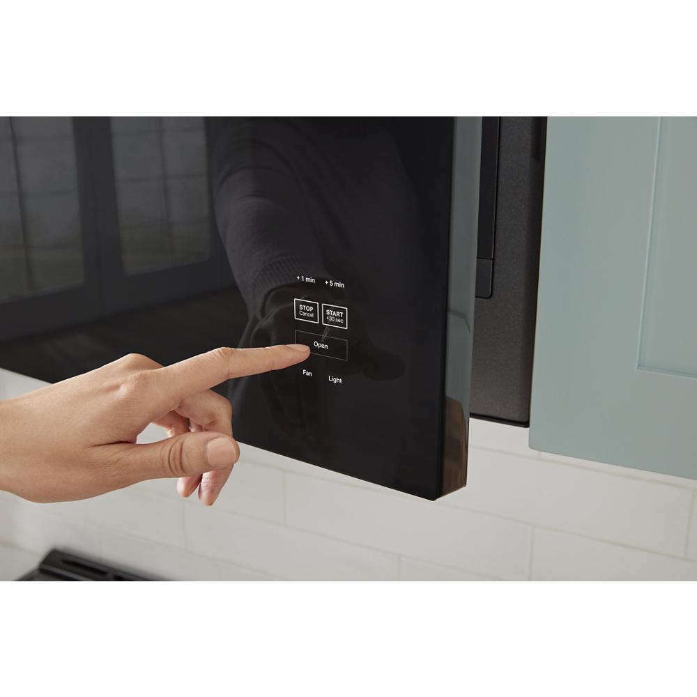 Hand pressing control panel on built-in microwave with black glass front in modern kitchen setting