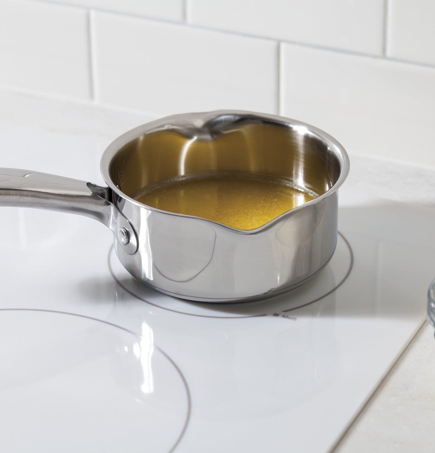 Stainless steel saucepan with liquid heating on a white built-in electric cooktop in kitchenware collection