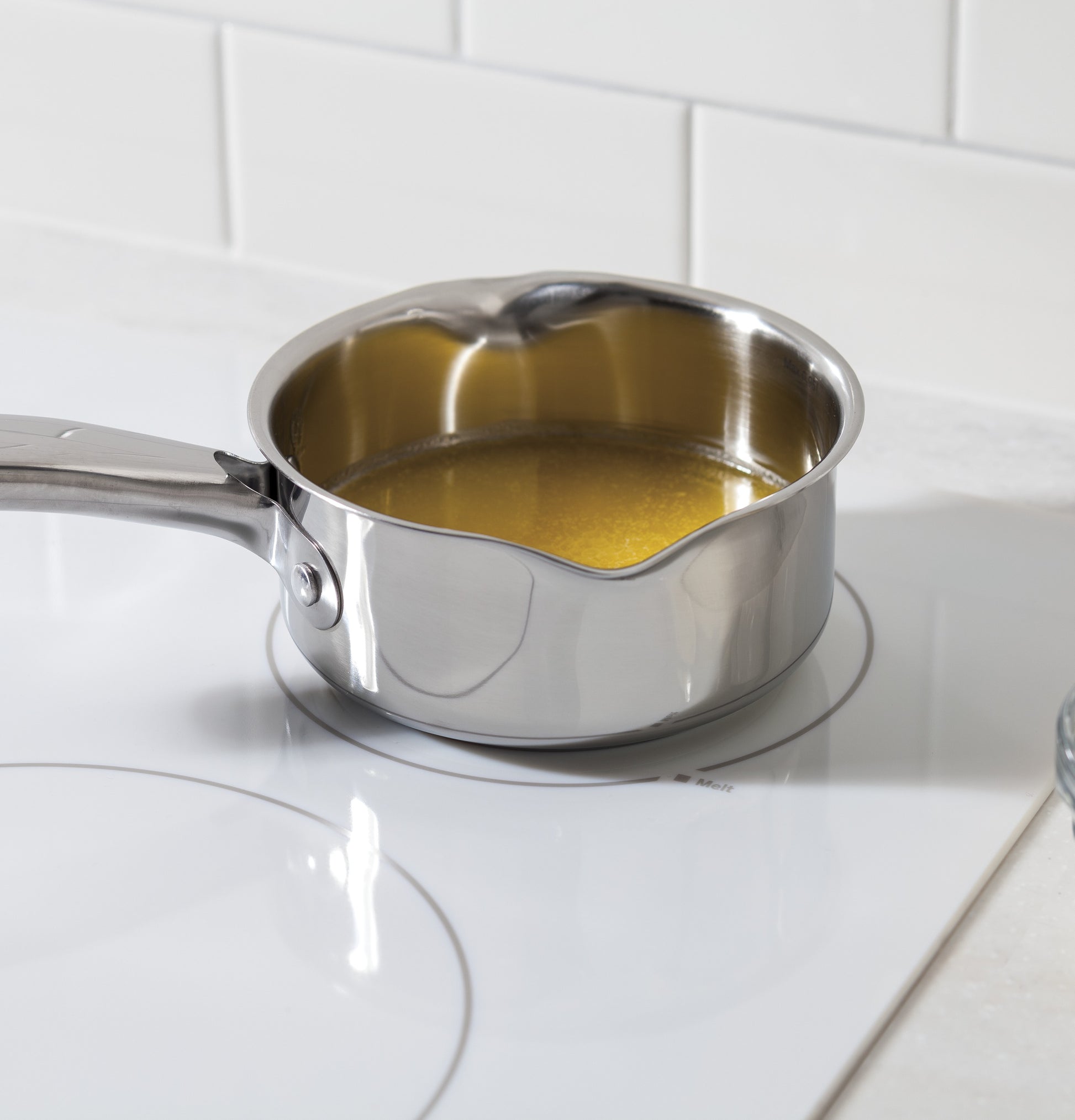 Stainless steel saucepan with liquid heating on a white built-in electric cooktop in kitchenware collection