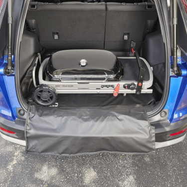 Compact portable grill secured in a vehicle trunk with a black cargo protector for tools and home improvement use