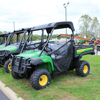 Green John Deere utility vehicle with overhead canopy and rugged tires parked outdoors on grassy display area