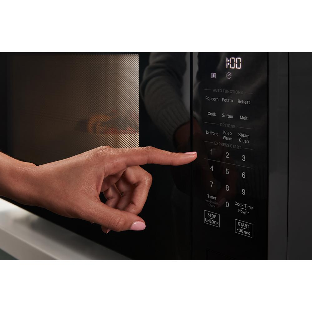 Finger pressing digital keypad on black sensor cooking microwave control panel in modern kitchen setting
