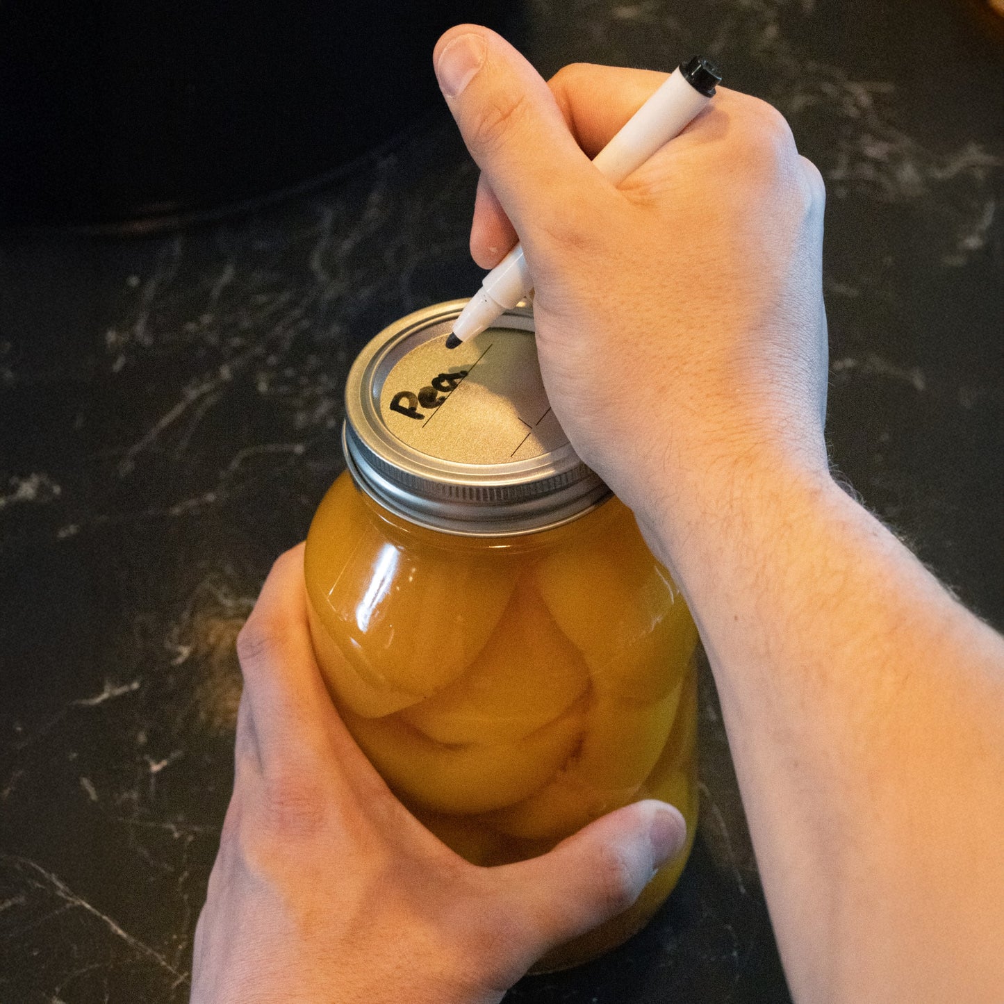 Hands labeling a glass jar sealed with silver-tone regular-mouth canning lid in kitchenware collection under $25