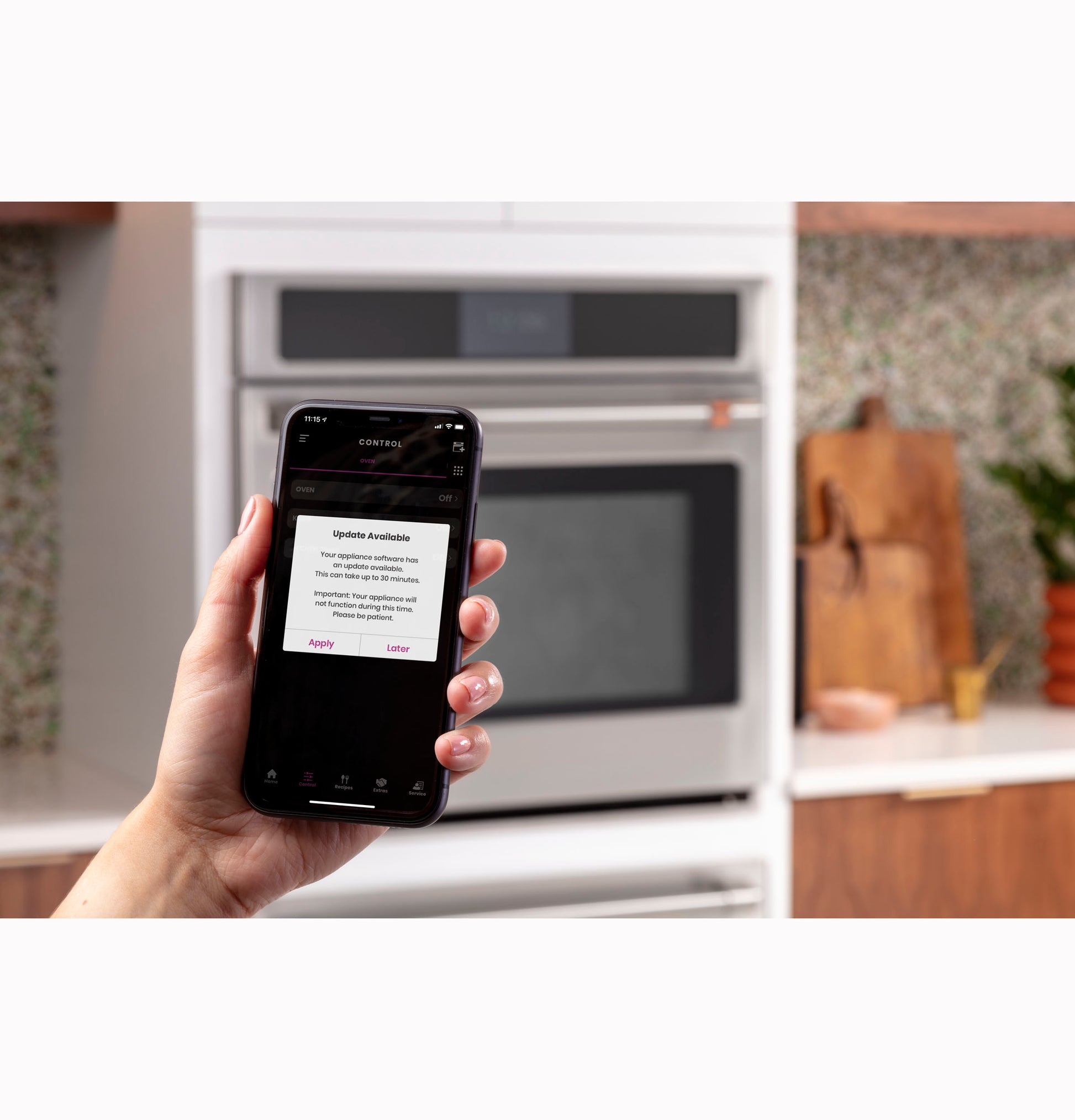 Hand holding smartphone displaying appliance update notification in modern kitchen with wall oven in background