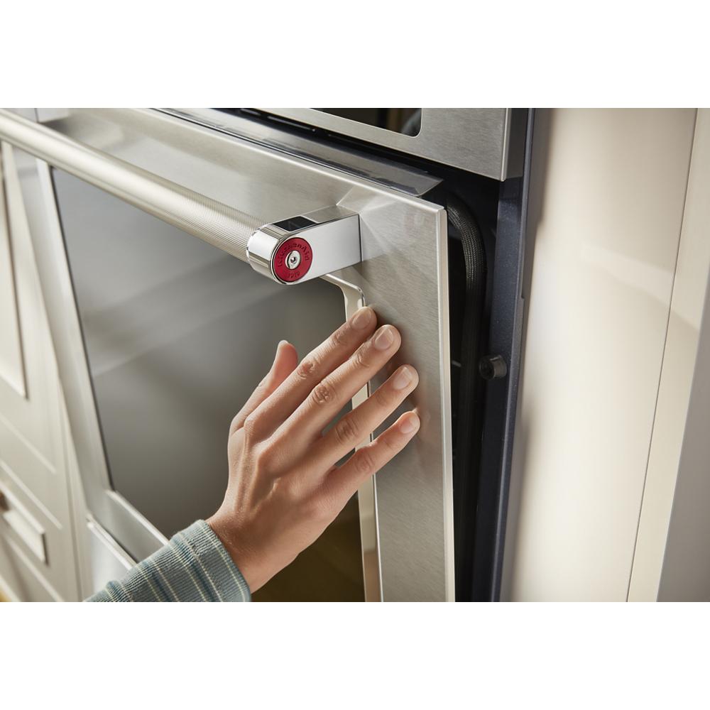 Hand grasping the handle of a stainless steel 24-inch smart single wall oven door in kitchen setting