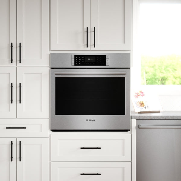 Built-in stainless steel wall oven with digital display, integrated into modern white kitchen cabinetry with black hardware