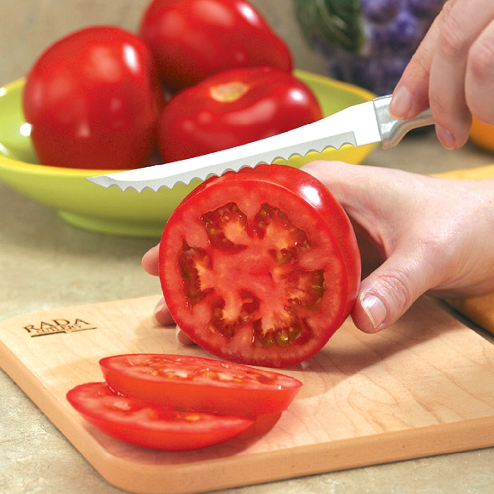 Serrated knife with a solid aluminum handle slicing a fresh tomato on a wooden cutting board, ideal for Kitchenware and Cooking Utensils collections.