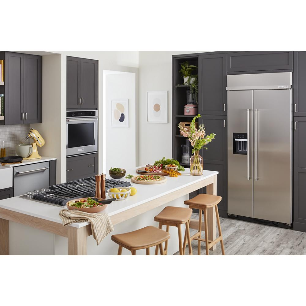 Modern kitchen with stainless steel side-by-side refrigerator, dark cabinetry, white island, and wooden stools in KitchenAid appliances collection