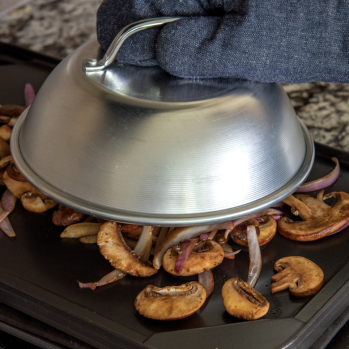 Aluminum cheese melting dome with handle covering mushrooms and onions on electric griddle for kitchen gadgets and tools