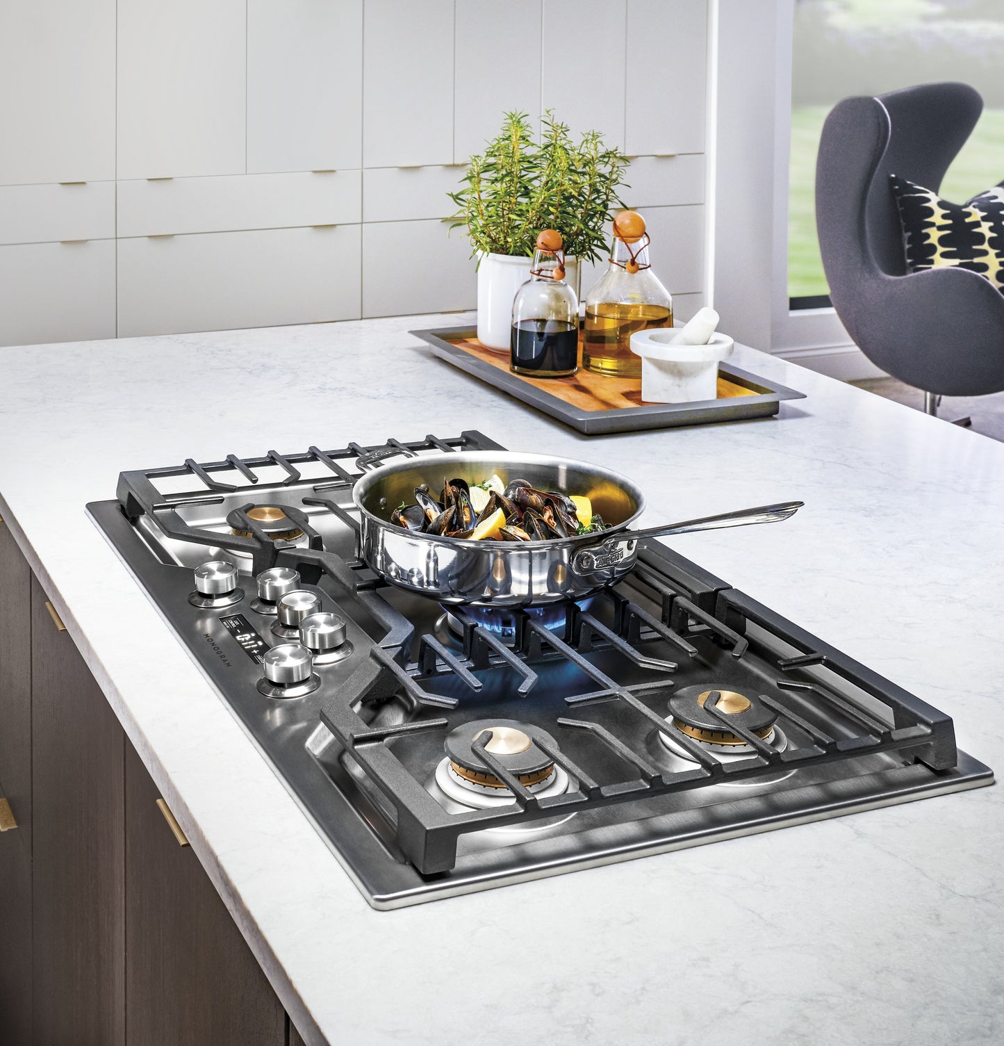 Stainless steel cooktop with deep-recessed burners and cast iron grates cooking mussels on a modern kitchen island