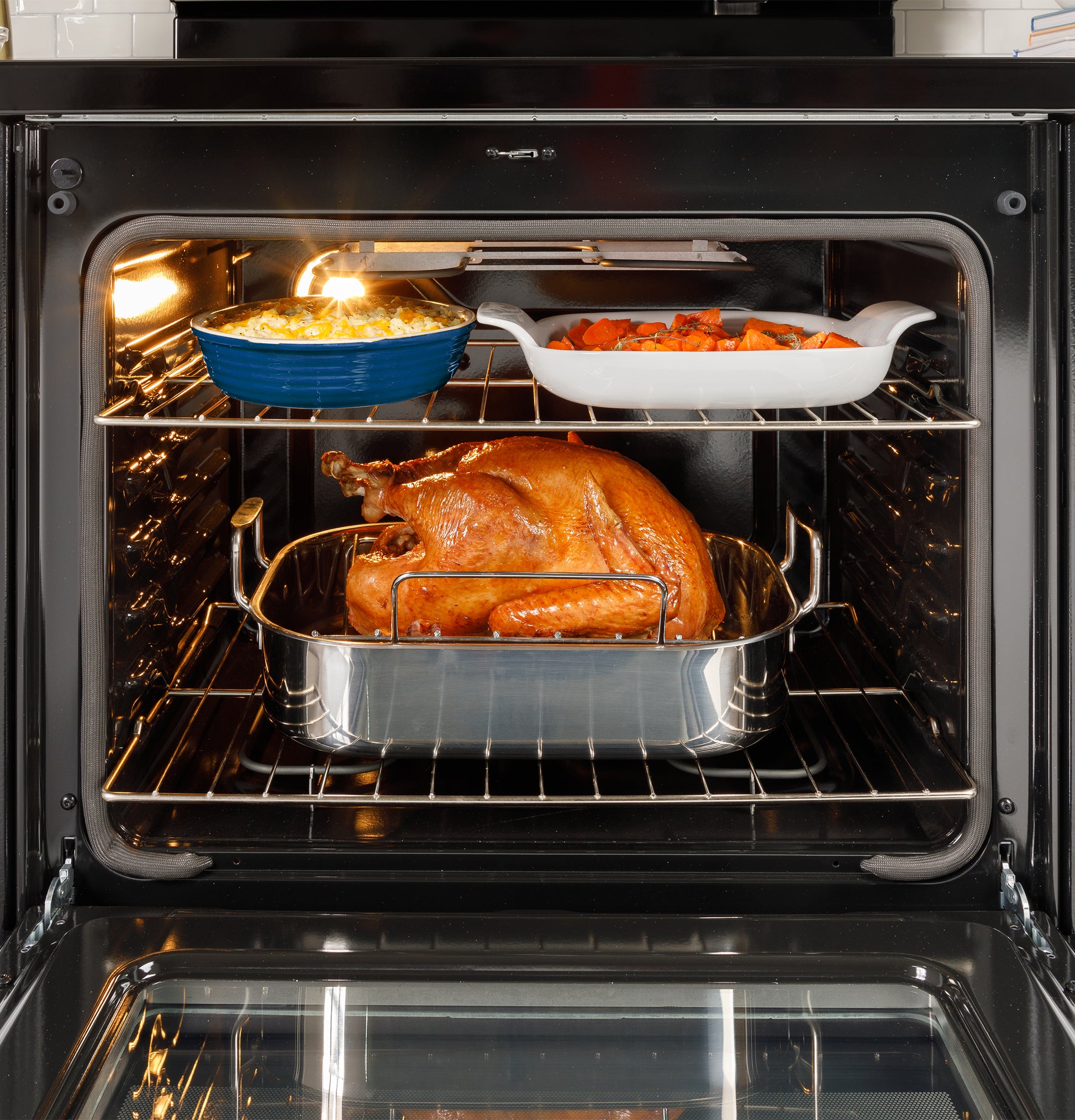 Roast turkey cooking inside electric oven with two casserole dishes containing side dishes on upper rack