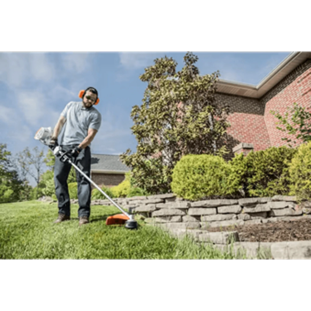 Man trimming lawn near brick house using STIHL straight shaft bike-handle trimmer for home improvement tasks