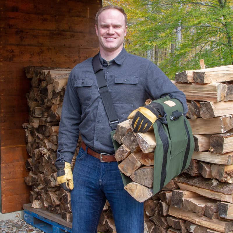 Man carrying heavy-duty green LogOX WoodOX Sling Firewood Carrier filled with split logs for home improvement tasks
