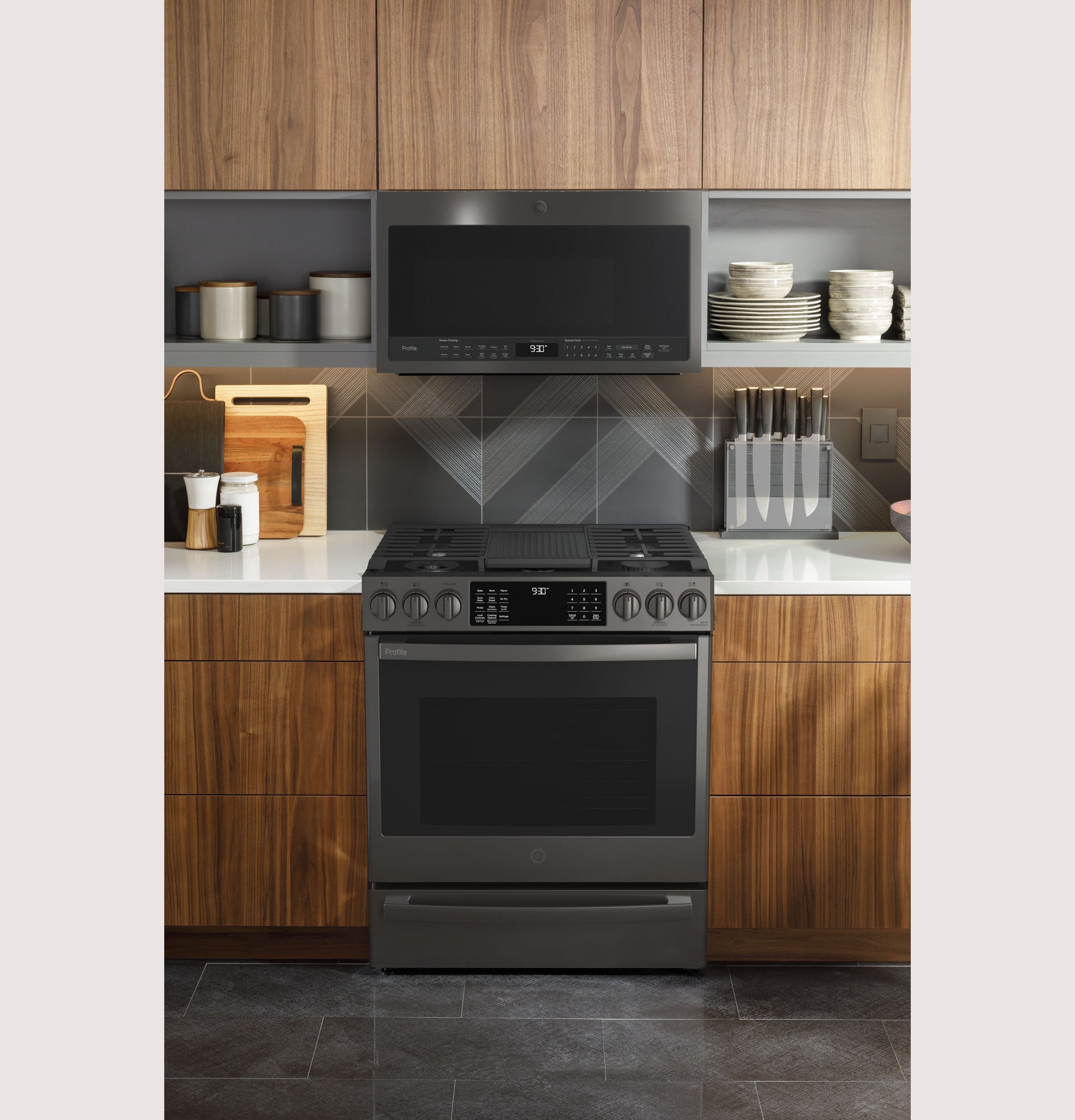 Modern dark stainless steel slide-in gas range with digital controls in a kitchen featuring wood cabinets and open shelving.