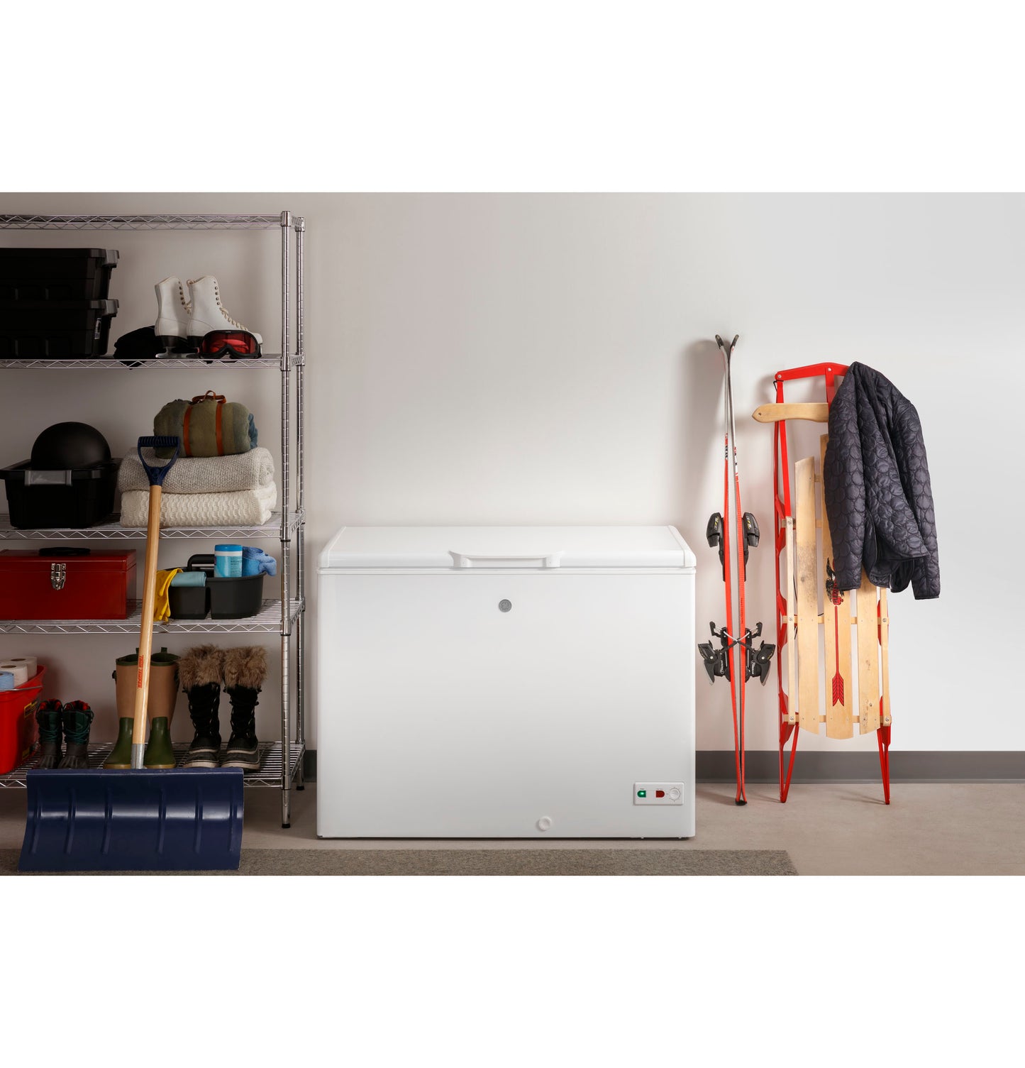 White manual defrost chest freezer in garage setting with winter gear, tools, and storage shelves nearby