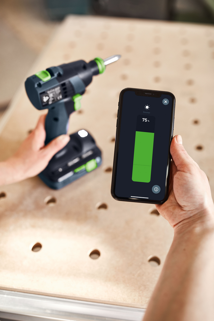 Person holding a Festool 576901 TXS 18 cordless drill and smartphone displaying tool settings for woodworking tasks