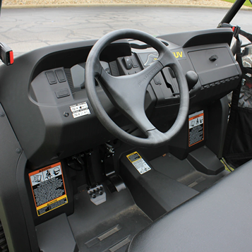 Interior view of mid-size utility vehicle dashboard featuring steering wheel and control pedals for outdoor tasks