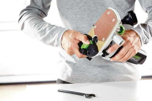 Person adjusting a Festool trim router with ergonomic handle for precise woodworking home improvement tasks